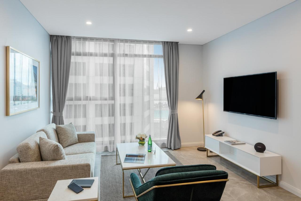 Meriton Suites Sussex Street, Sydney Buitenkant foto The photo shows a modern living room space with a light, airy ambiance. It features a comfortable beige sofa with decorative cushions, a sleek coffee table placed in front, and a dark green armchair. There is a large window covered with sheer curtain
