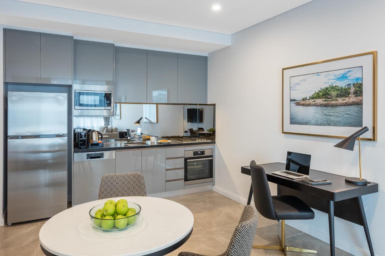 Meriton Suites Sussex Street, Sydney Buitenkant foto The photo shows a modern kitchen and dining area in an apartment. The kitchen features sleek gray cabinetry, a stainless steel fridge, and a microwave. There is a countertop with cooking appliances, including an oven and stovetop. A small round dinin