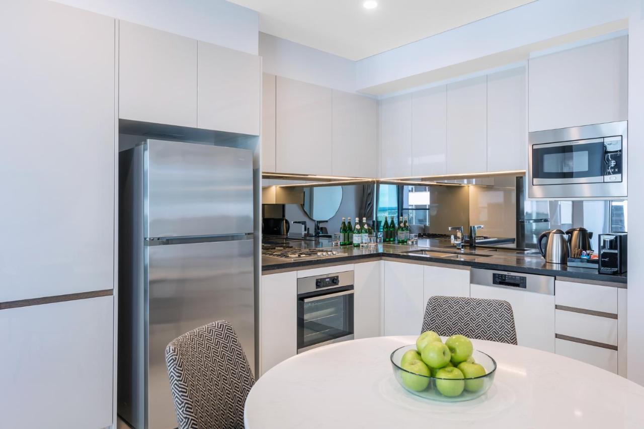 Meriton Suites Sussex Street, Sydney Buitenkant foto The photo displays a modern kitchen with a sleek design. It features light-colored cabinetry and a countertop with a polished finish. On the left, there is a stainless steel refrigerator. The kitchen is equipped with various appliances, including an 