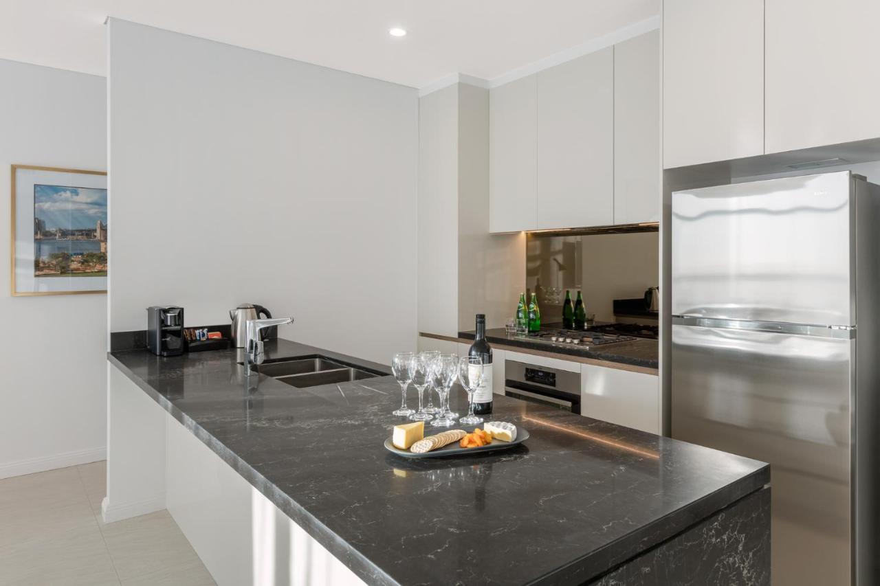 Meriton Suites Sussex Street, Sydney Buitenkant foto The photo shows a modern kitchen featuring a sleek design with a dark stone countertop. There is a built-in sink and possibly a cooktop. The kitchen cabinetry is light-colored, creating a contrast with the dark counter. On the countertop, there are w