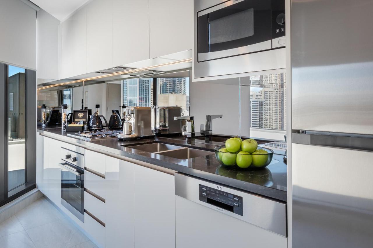 Meriton Suites Sussex Street, Sydney Buitenkant foto The photo shows a modern kitchen featuring sleek cabinetry and stainless steel appliances. There is a glossy countertop with a bowl of green apples as a decoration. The kitchen includes a built-in oven, a microwave, and other kitchen gadgets, along w