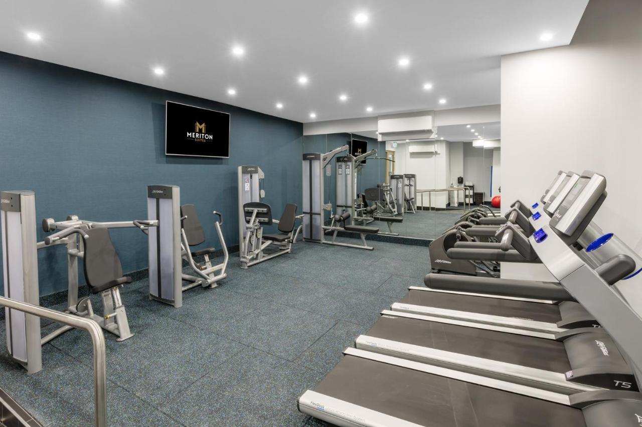 Meriton Suites Sussex Street, Sydney Buitenkant foto The photo shows a modern gym interior. The space features several pieces of exercise equipment, including weight machines and stationary bikes. The walls are painted a calming color, and the flooring is carpeted. There are also mirrors on the walls, 