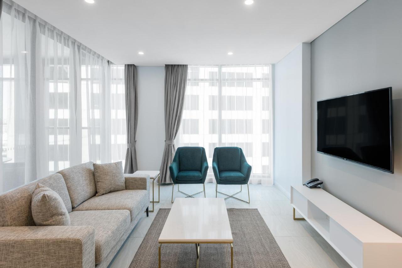 Meriton Suites Sussex Street, Sydney Buitenkant foto The photo shows a modern living room equipped with a light gray sofa, two teal chairs, and a coffee table in the center. The room features large windows with sheer curtains, allowing natural light to illuminate the space. There is a white media conso
