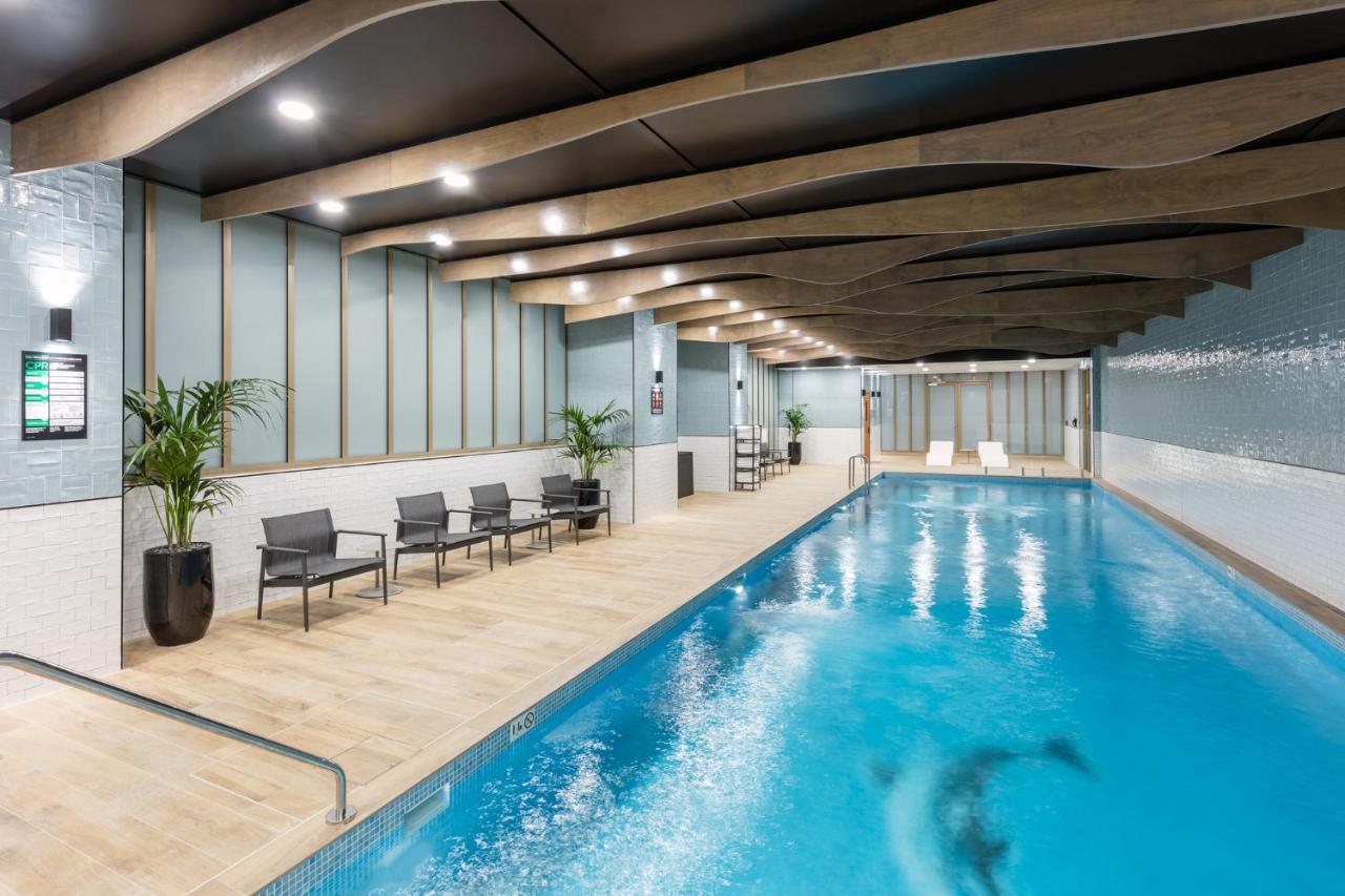 Meriton Suites Sussex Street, Sydney Buitenkant foto The photo shows an indoor swimming pool area. The pool has clear blue water and is flanked by a wooden deck. There are several lounge chairs arranged along one side of the pool. The ceiling features a modern design with wooden beams and recessed ligh