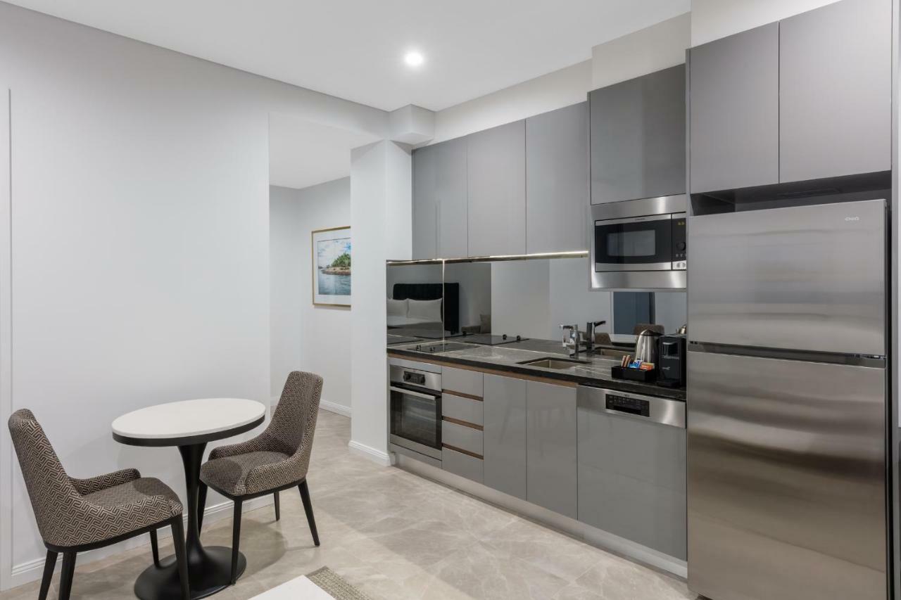 Meriton Suites Sussex Street, Sydney Buitenkant foto The photo shows a modern kitchen area that features a sleek design. The cabinetry and appliances are in shades of gray, giving it a contemporary look. There is a stainless steel refrigerator, microwave, and oven, along with a sink and cooking area. 
